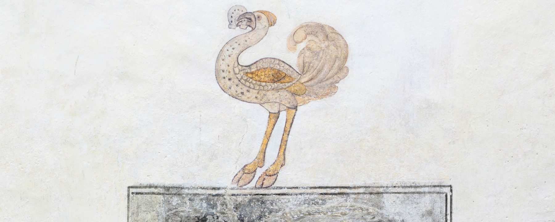 Fassadendetail: Strauss mit Hufeisen im Schnabel.