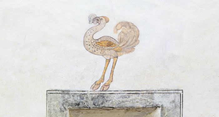 Fassadendetail: Strauss mit Hufeisen im Schnabel.